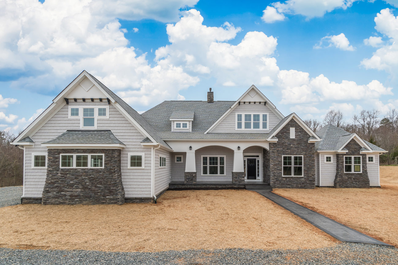 A finished craftsman custom home with wide stone porch columns, photographed from the front lawn