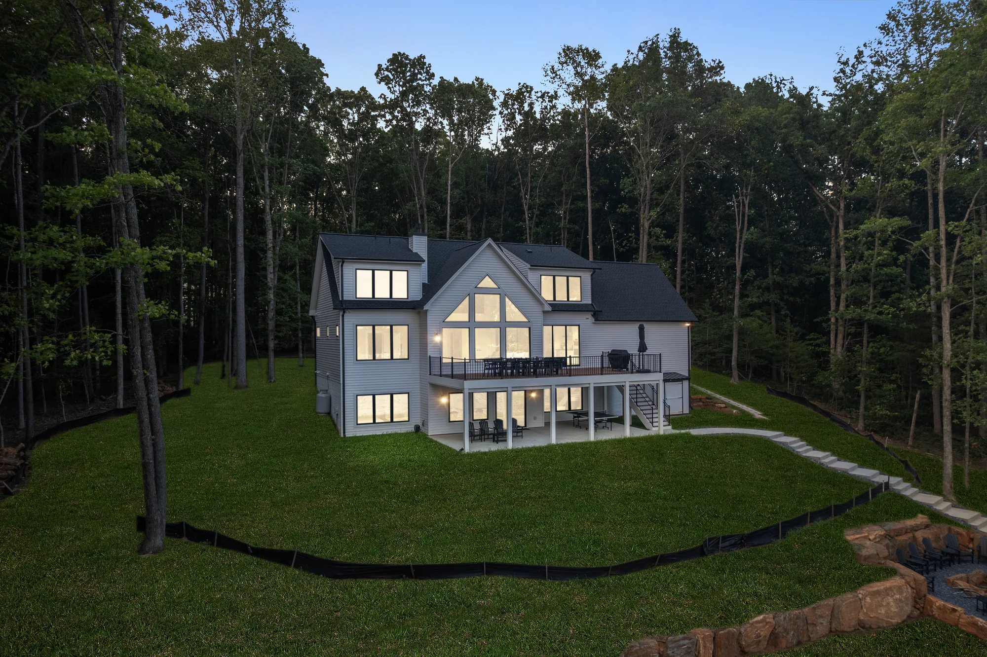 Twilight aerial of the rear elevation of a Spartan Homes lakefront custom home on a wooded Lake Anna, Virginia lot with lit windows.