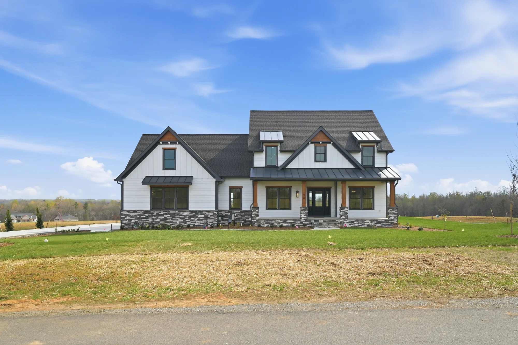 A Spartan Homes custom white farmhouse with a stone base and black roof under a blue sky near Lake Anna, Virginia