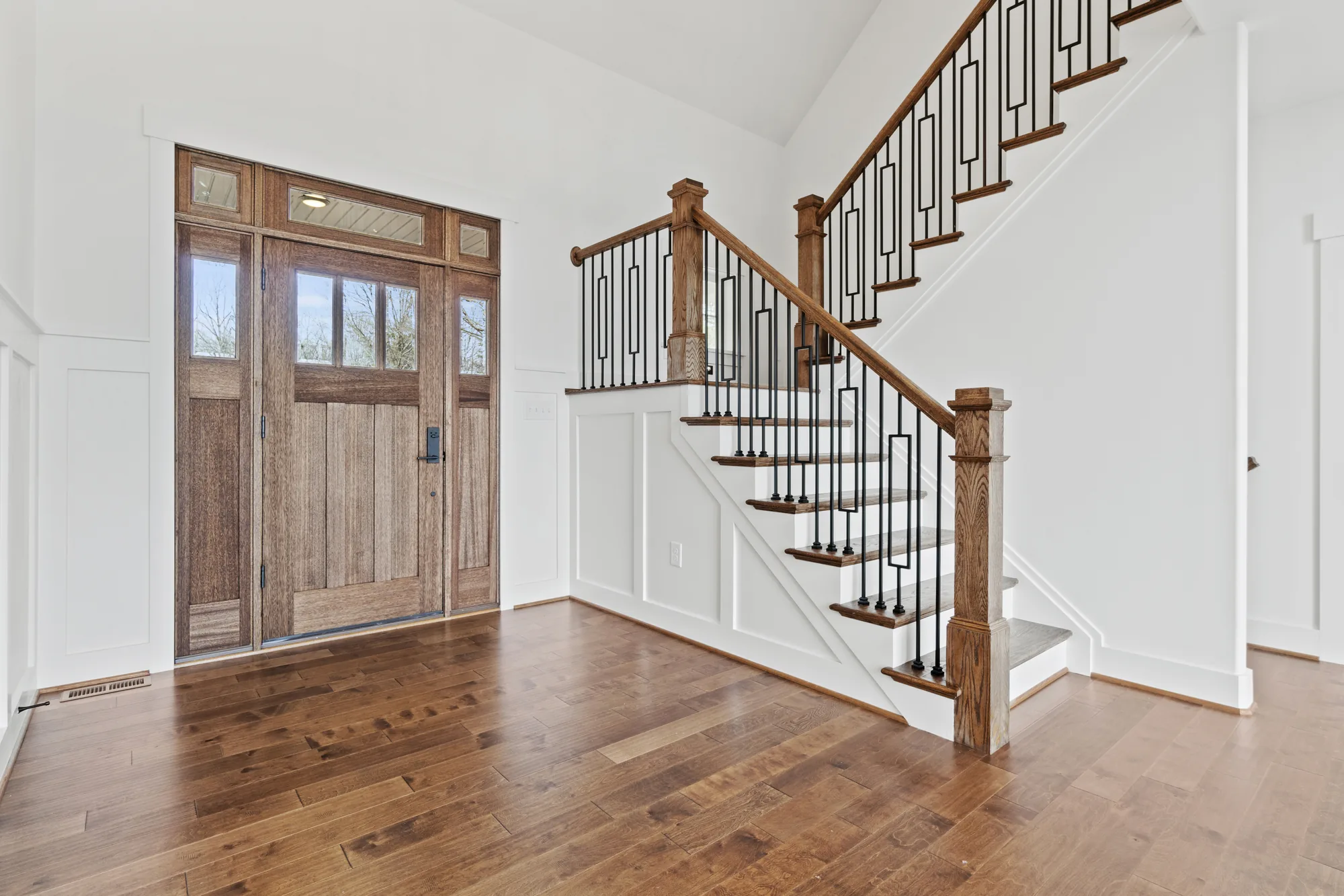 A Spartan Homes foyer with a wood front door and a staircase with a wrought-iron railing