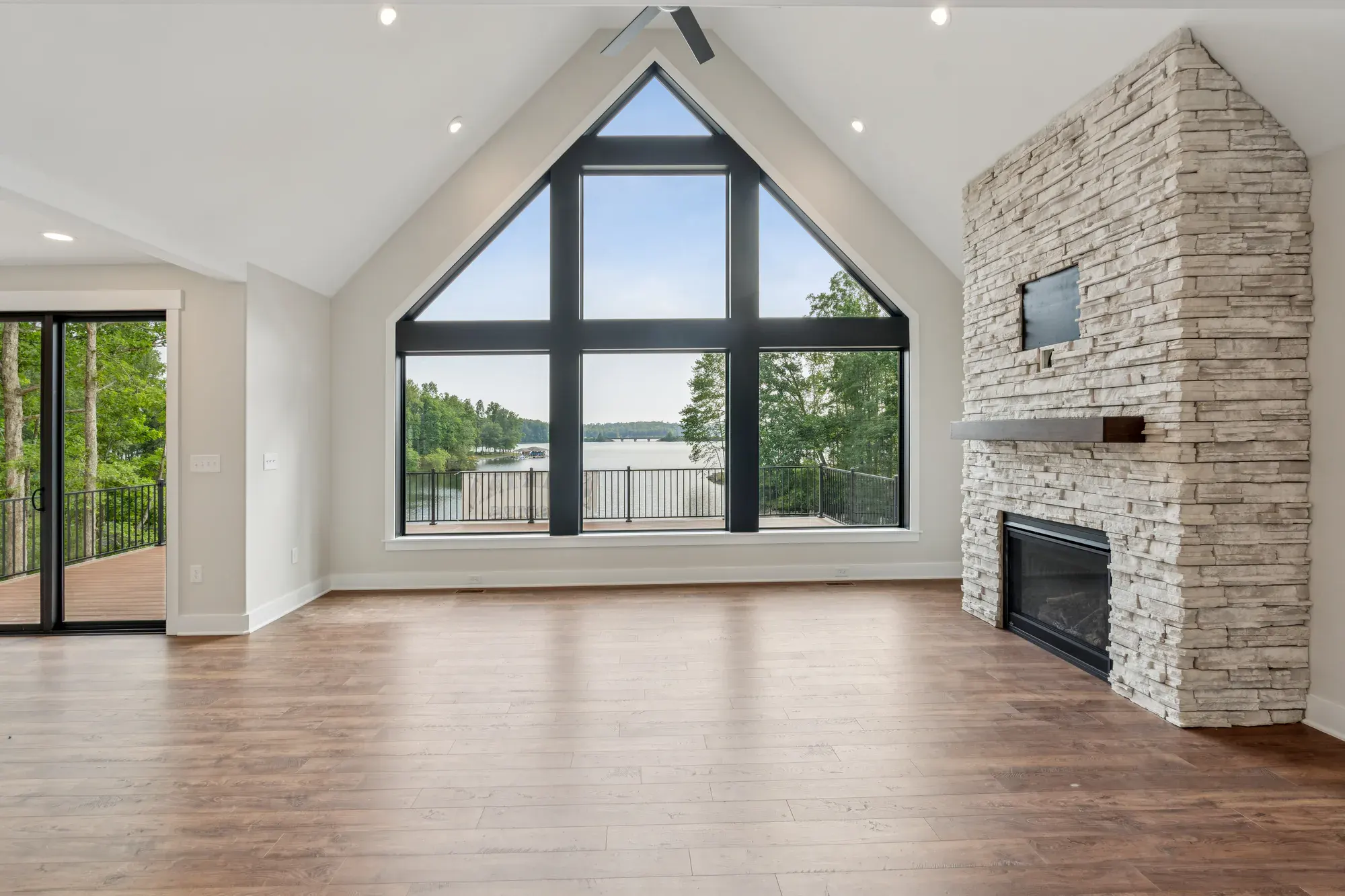 A Spartan Homes great room with a stone fireplace and a floor-to-ceiling triangular window wall framing the lake view