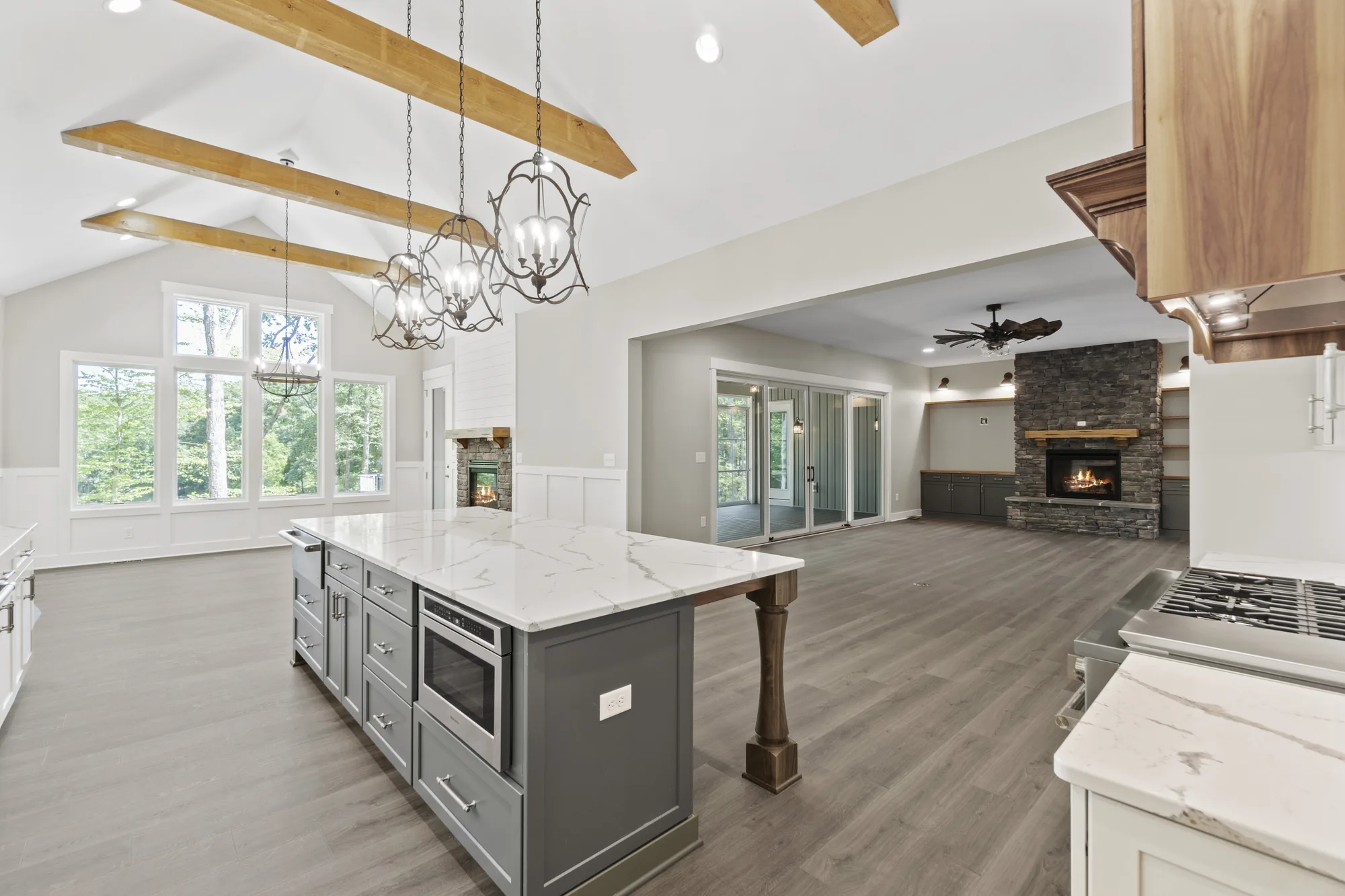 A Spartan Homes custom kitchen with a vaulted beamed ceiling, a large marble island and chandeliers, with a stone fireplace beyond