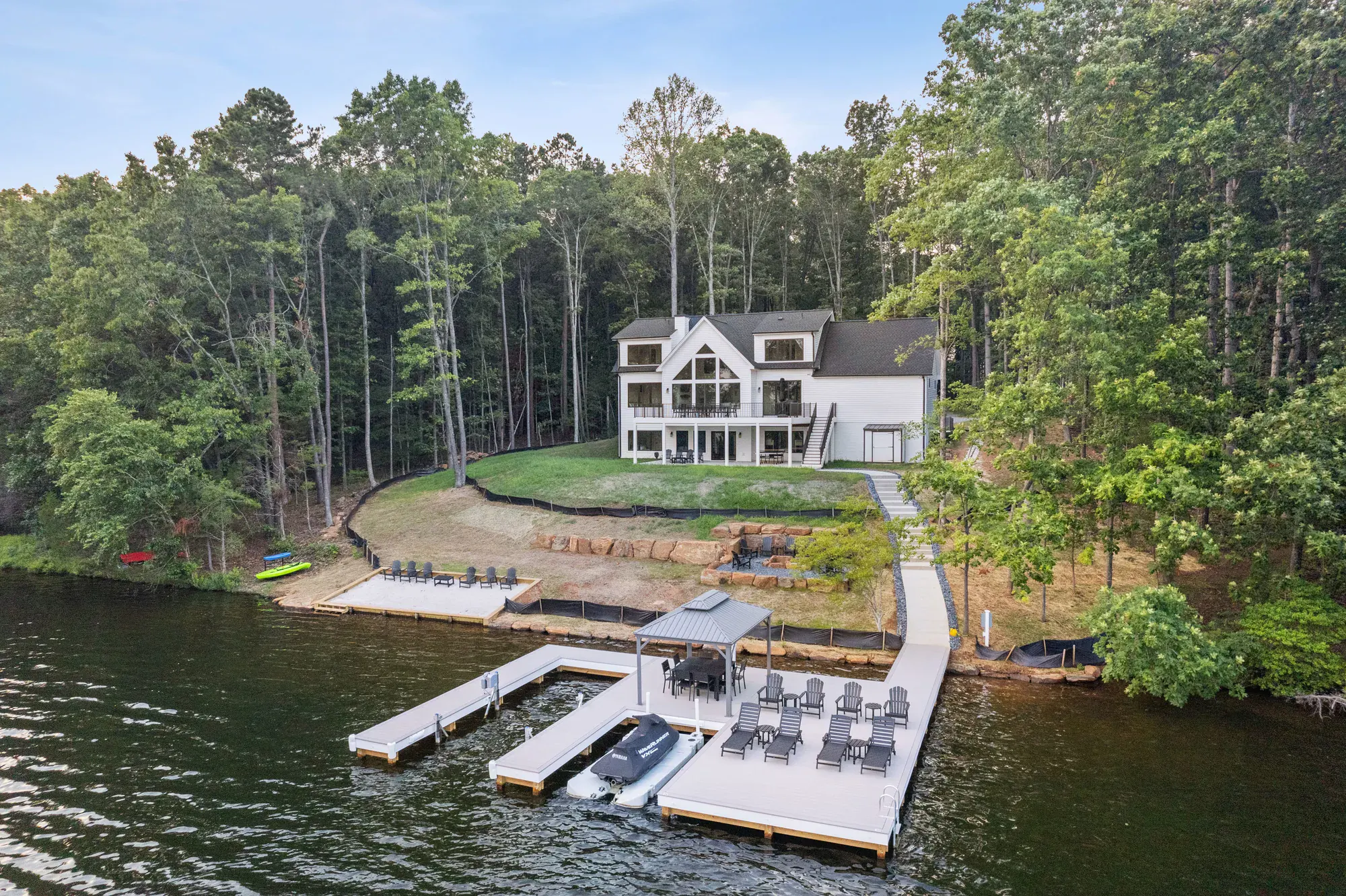An aerial view of a Spartan Homes custom home with a double dock, lawn and shoreline on a sunny day at Lake Anna, Virginia