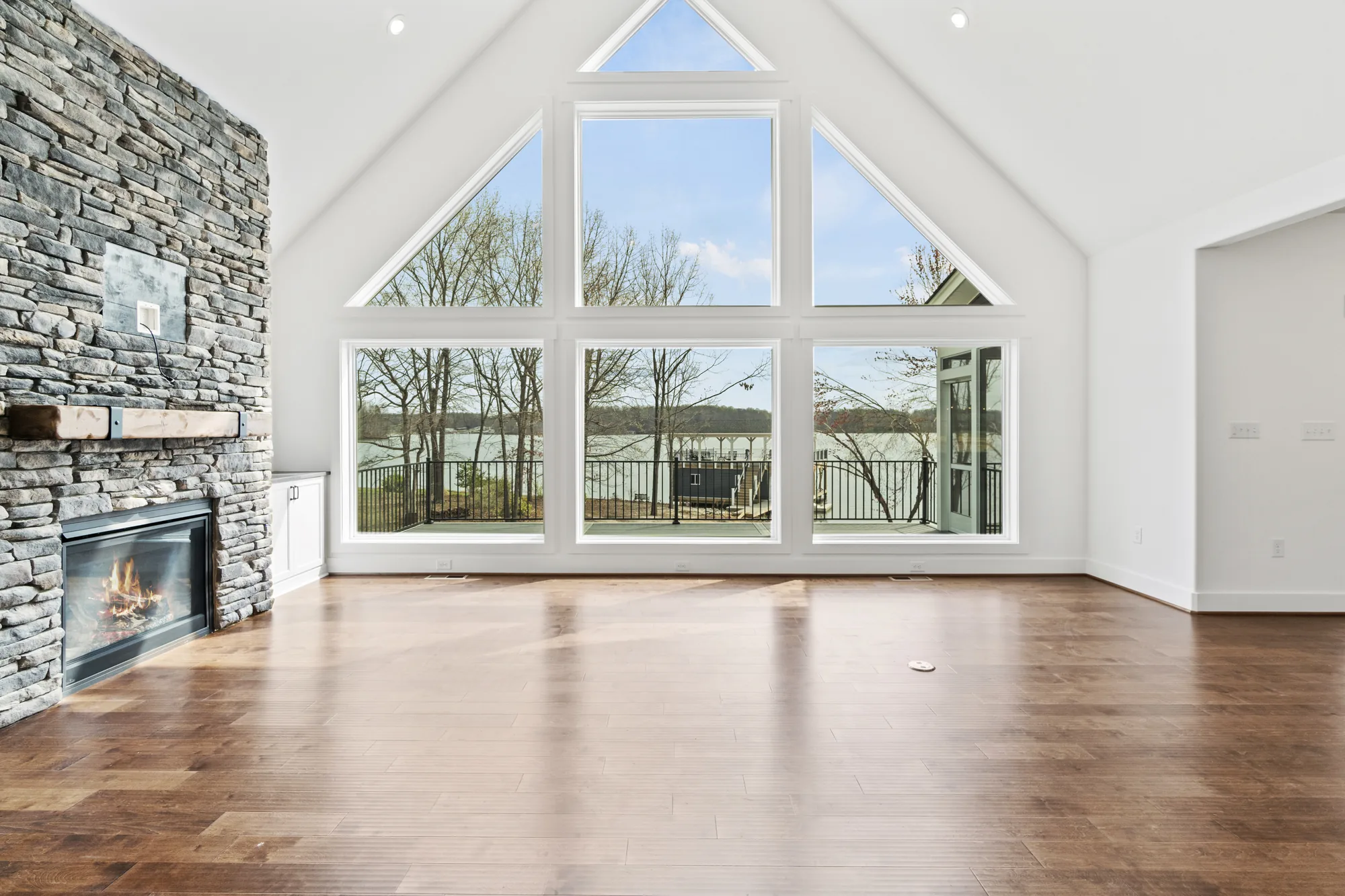 Living room with a stone fireplace and a floor-to-ceiling window wall framing Lake Anna at a Spartan Homes lakefront custom home in Virginia.