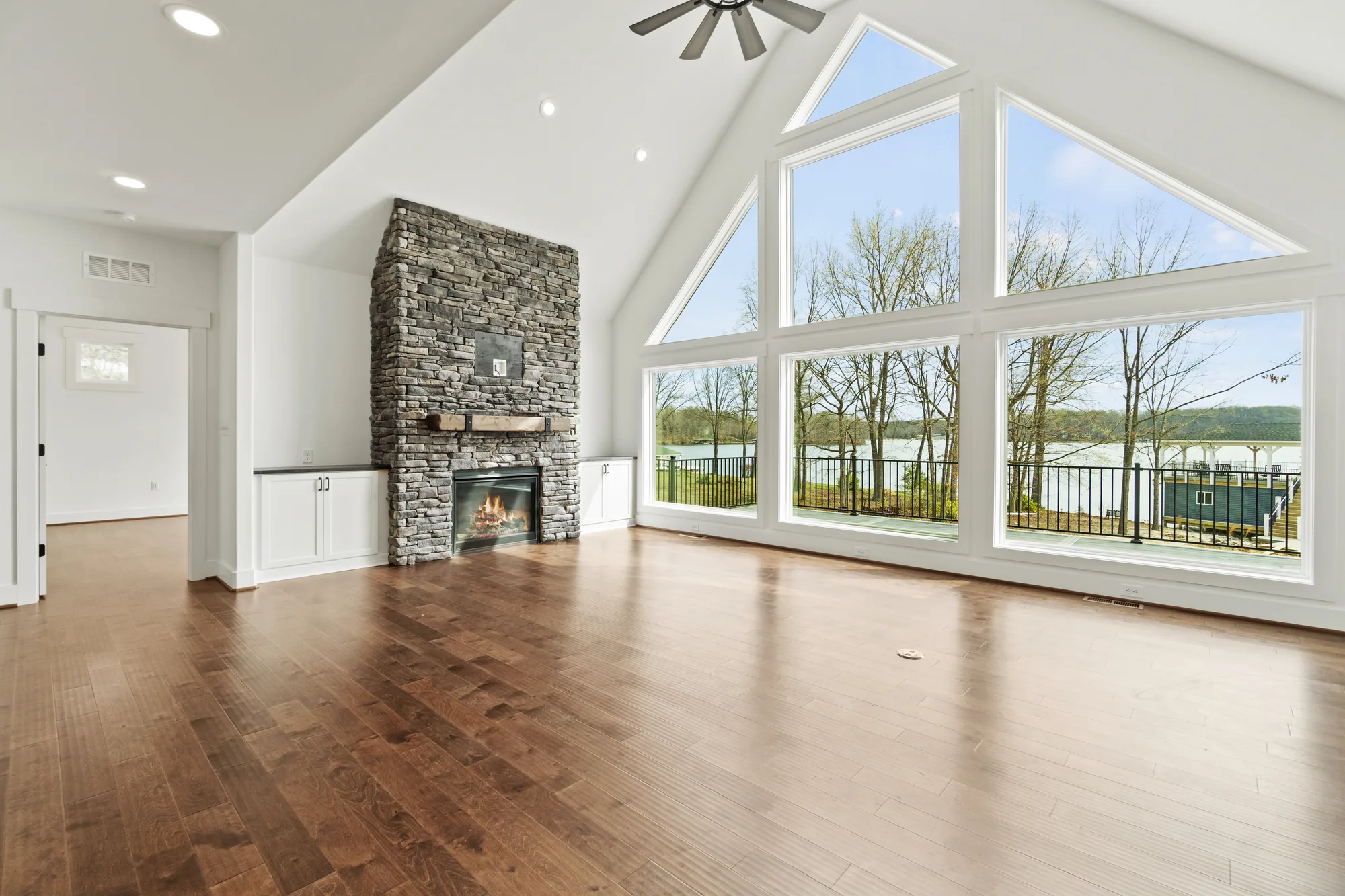 Vaulted living room with a ceiling fan, stone fireplace, and a wall of windows over Lake Anna at a Spartan Homes custom home in Virginia.