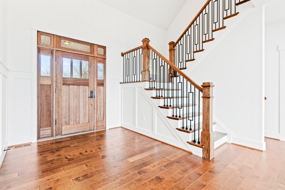 A custom home entry foyer with a solid wood front door and an open staircase rising to the second floor