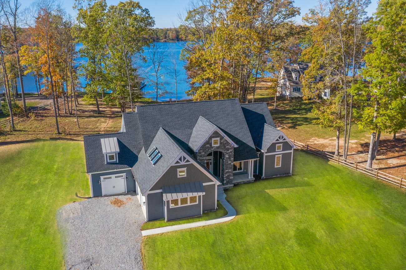 An aerial view of a craftsman custom home on a wooded lot running down to the water at Lake Anna